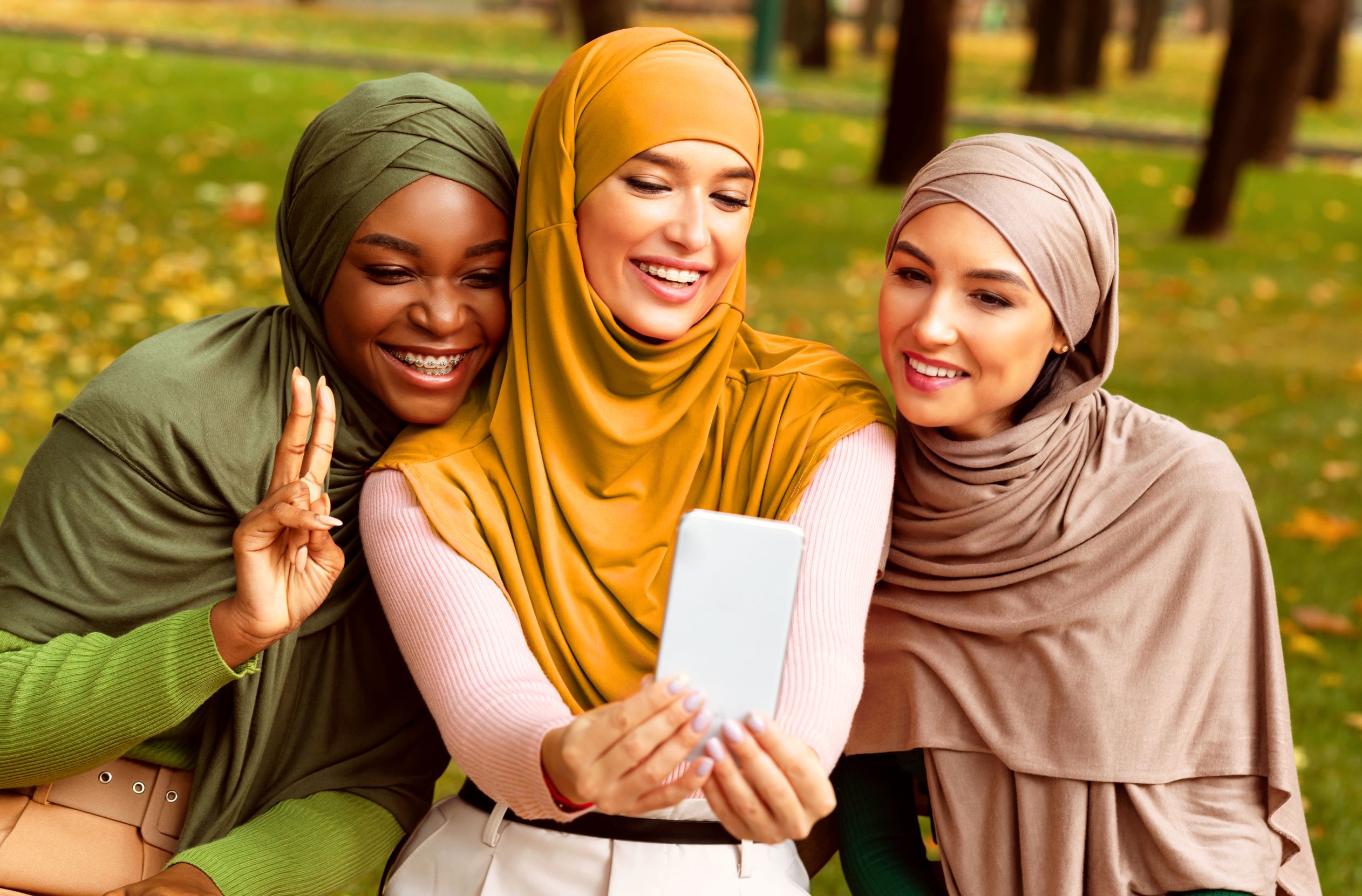 Three women seating next to each other in the park taking a selfie.