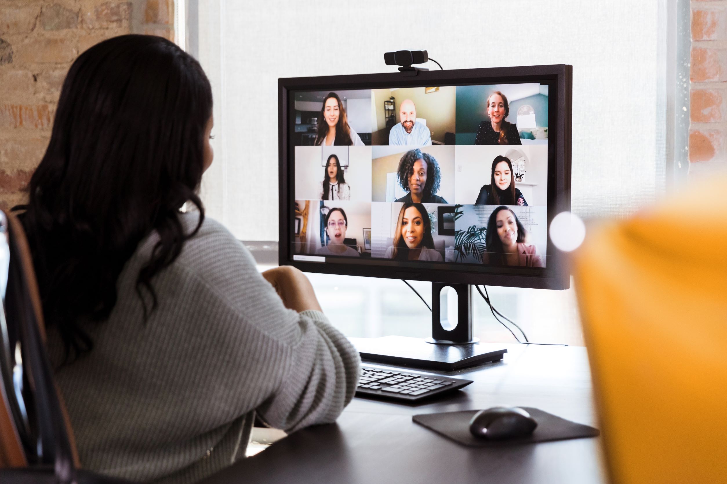 Woman seating at her desk looking at a computer screen and participating on a zoom call