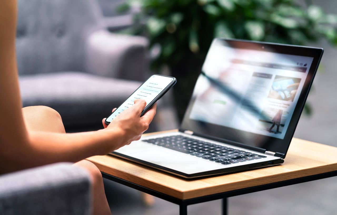 POV shot of woman holding phone in front of laptop